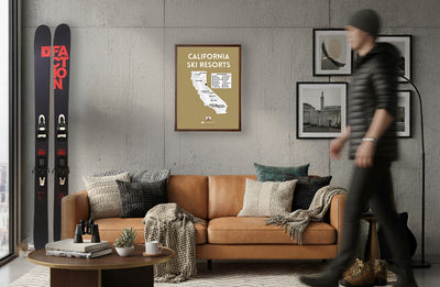 Living room with brown leather sofa, coffee table, and wall art including skis and a map of California ski resorts.