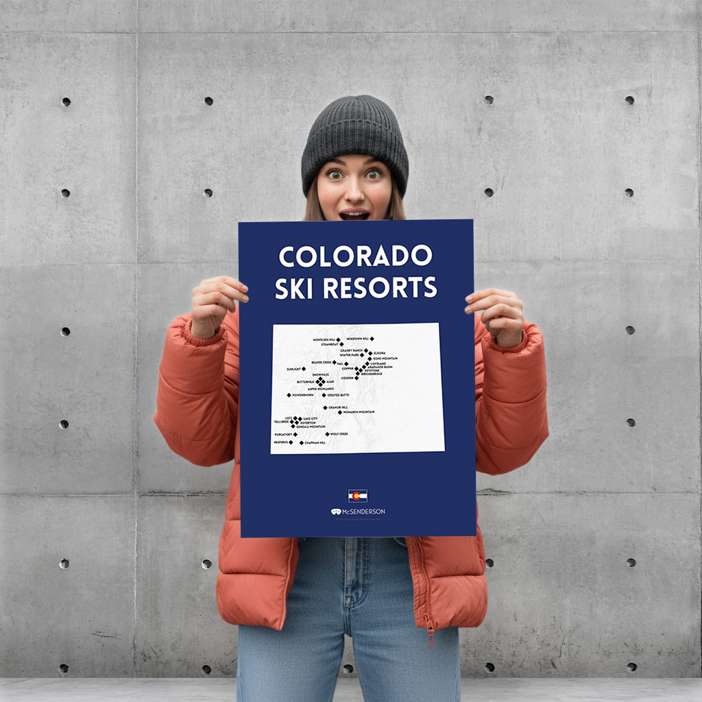 Person holding a scratch off poster titled 'Colorado Ski Resorts' against a concrete wall.