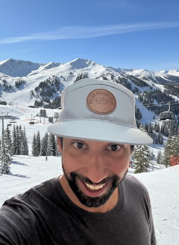 Man wearing a light blue McSenderson 5-panel hat with a logo indoors, smiling at the camera.