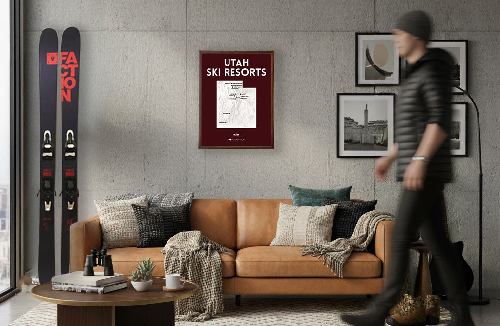 Living room with brown leather sofa, coffee table, and wall art including skis and 'Utah Ski Resorts' poster.